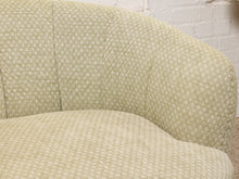 Load image into Gallery viewer, Image 10 of 16: Close-up of a curved upholstered armchair or sofa section with a light beige and white textured woven fabric against a white brick wall.
