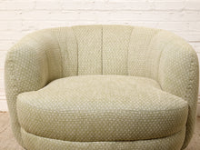 Load image into Gallery viewer, Image 12 of 16: A round upholstered accent chair in a light sage green fabric with a small repeating geometric pattern, set against a white brick wall background.
