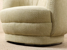 Load image into Gallery viewer, Image 14 of 16: Close-up of a round upholstered chair or swivel armchair in a light beige fabric with a small repeating geometric pattern, showing the seat cushion and side upholstery.
