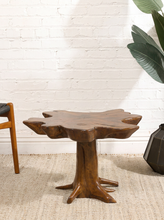 Load image into Gallery viewer, Image 3 of 16: Sculptural wood coffee table featuring a thick, irregularly shaped freeform tabletop with a warm brown finish, organic curved edges, and a branching tree root-style pedestal base.
