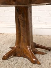 Load image into Gallery viewer, Image 13 of 16: Close-up of a rustic wooden table base shaped like a tree trunk with three claw-like feet, set on a woven rug against a white brick wall.
