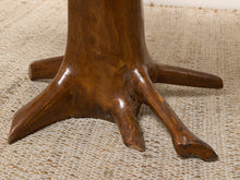Load image into Gallery viewer, Image 14 of 16: Close-up of a rustic wooden table base shaped like a tree trunk with three gnarled legs, resting on a woven beige rug.
