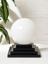 Load image into Gallery viewer, Image 1 of 22: Vintage table lamp with large round white glass globe shade and stepped black geometric pedestal base
