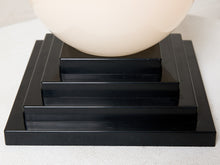 Load image into Gallery viewer, Image 14 of 22: Close-up of a black tiered rectangular base supporting a large off-white oval shade or bowl, photographed against a light neutral background.
