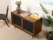 Load image into Gallery viewer, Image 3 of 24: Vintage wooden credenza with two black textured sliding cabinet doors, warm brown wood frame, gold-tone hardware, and short tapered legs
