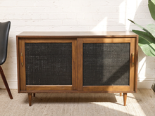 Load image into Gallery viewer, Image 4 of 24: Vintage wooden credenza with two black textured sliding cabinet doors, warm brown wood frame, gold-tone hardware, and short tapered legs
