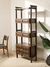Load image into Gallery viewer, Image 5 of 25: Vintage dark wood étagère bookshelf featuring three open display shelves, two drawers with raised rectangular panel details, a lower double-door cabinet with geometric square panels, and round cream-colored knobs.
