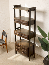 Load image into Gallery viewer, Image 6 of 25: Vintage dark wood étagère bookshelf featuring three open display shelves, two drawers with raised rectangular panel details, a lower double-door cabinet with geometric square panels, and round cream-colored knobs.
