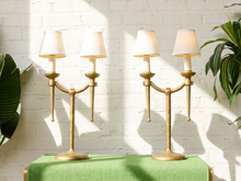 Load image into Gallery viewer, Image 1 of 21: Pair of vintage gold-tone metal table lamps, each featuring two gracefully curved arms, candle-style light fittings, smooth ivory tapered fabric shades, a slender central stem, and a rounded pedestal base.
