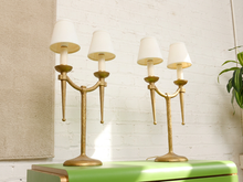 Load image into Gallery viewer, Image 5 of 21: Pair of vintage gold-tone metal table lamps, each featuring two gracefully curved arms, candle-style light fittings, smooth ivory tapered fabric shades, a slender central stem, and a rounded pedestal base.
