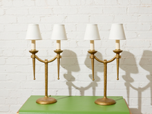 Load image into Gallery viewer, Image 7 of 21: Pair of vintage gold-tone metal table lamps, each featuring two gracefully curved arms, candle-style light fittings, smooth ivory tapered fabric shades, a slender central stem, and a rounded pedestal base.
