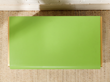 Load image into Gallery viewer, Image 7 of 16: A rectangular lime green yoga mat with light wood edges, laid flat on a beige woven jute rug with a white painted wooden floor visible at the top.
