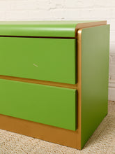 Load image into Gallery viewer, Image 8 of 16: A close-up of a two-drawer dresser with bright green painted fronts and a natural wood frame, set against a white brick wall and light woven rug.
