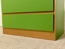 Load image into Gallery viewer, Image 14 of 16: A close-up of a green and tan wooden dresser or cabinet, showing two green drawer fronts and a tan base, set on a beige carpeted floor.
