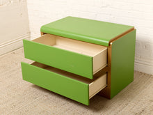 Load image into Gallery viewer, Image 15 of 16: A mid-century modern two-drawer nightstand in bright green with a gold-tone metal frame, shown with both top and front drawers open, set against a white brick wall and beige carpet.
