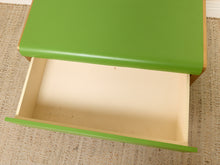 Load image into Gallery viewer, Image 16 of 16: A close-up of a green drawer with its front panel pulled open, showing the light wood interior and drawer front edge, set on a woven beige rug.
