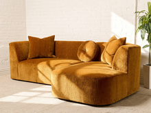 Load image into Gallery viewer, Image 3 of 16: Bonnie Two-Piece Sectional Sofa in Thriller Amber featuring golden amber textured upholstery, rounded arms, generously cushioned seating, a right-facing curved chaise, two square accent pillows, and a matching round tufted pillow.
