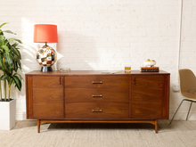 Load image into Gallery viewer, Image 2 of 24: Vintage mid-century modern walnut credenza by Kroehler Furniture featuring three central drawers with brass-tone horizontal pulls, two side cabinet doors with vertical handles, richly figured walnut wood grain, and slender tapered wooden legs.
