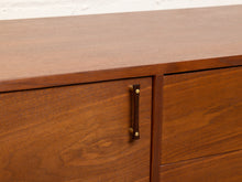 Load image into Gallery viewer, Image 10 of 24: Close-up of a mid-century modern wooden sideboard or credenza with warm brown walnut-like wood grain and a dark metal vertical handle with brass accents.
