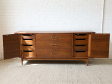 Load image into Gallery viewer, Image 20 of 24: Mid-century modern walnut wood sideboard cabinet with open doors and multiple drawers, set against a white brick wall and light rug.
