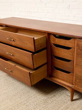 Load image into Gallery viewer, Image 23 of 24: Mid-century modern wooden sideboard with multiple drawers, shown with several drawers pulled open against a white brick wall and textured carpet.
