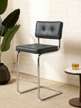 Load image into Gallery viewer, Image 1 of 17: 1970s-style counter stool featuring black button-tufted upholstered seat and backrest, polished chrome tubular cantilever frame, curved sled-style base, and integrated metal footrest.

