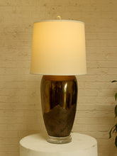 Load image into Gallery viewer, Image 6 of 17: Vintage table lamp featuring a tall rounded body with a reflective dark metallic upper finish, textured charcoal lower section, clear Lucite-style circular base, and illuminated ivory cylindrical drum shade.
