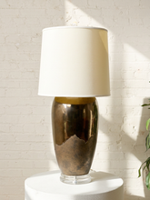 Load image into Gallery viewer, Image 5 of 17: Vintage table lamp featuring a tall rounded body with a reflective dark metallic upper finish, textured charcoal lower section, clear Lucite-style circular base, and illuminated ivory cylindrical drum shade.
