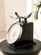 Load image into Gallery viewer, Image 2 of 10: Vintage mechanical weighing scale featuring a black metal body, raised metal weighing platform, large circular cream dial with black measurement markings, red pointer, and polished silver-tone rim.
