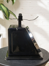Load image into Gallery viewer, Image 4 of 10: A vintage black metal cash register or counter with curved metal arms on top, displayed on a round black table against a white brick wall with a green plant leaf in the upper left.
