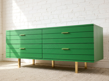 Load image into Gallery viewer, Image 12 of 15: A bright green six-drawer dresser with slim gold metal handles and gold legs, positioned against a white brick wall on a light beige carpet.
