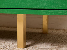 Load image into Gallery viewer, Image 13 of 15: Close-up of a green wooden table or bench with square gold-toned metal legs, shown standing on a beige woven rug against a light wall.
