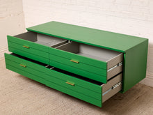 Load image into Gallery viewer, Image 14 of 15: A green floating storage cabinet with multiple drawers, some open to show gray interior compartments, set against a white brick wall and beige carpet.
