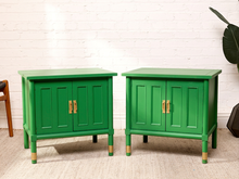 Load image into Gallery viewer, Image 1 of 21: Pair of vintage Kelly green cabinet nightstands featuring vibrant green painted finishes, vertical fluted side panels, two paneled cabinet doors each, brass-tone handles, square inset tops, and slender legs with brass-tone feet.
