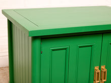 Load image into Gallery viewer, Image 12 of 21: A close-up of a green cabinet with paneled doors and gold-toned handles, shown against a light neutral background.

