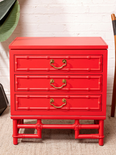 Load image into Gallery viewer, Image 7 of 21: A bright red three-drawer nightstand with a bamboo-inspired frame design and brass handles, set against a white brick wall background.
