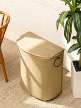 Load image into Gallery viewer, Vintage beige Atomic Age clothes hamper with rounded lid, brass-tone trim, textured patterned finish, and metal starburst accent
