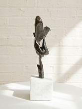 Load image into Gallery viewer, An abstract dark bronze sculpture on a white marble base, displayed on a white table against a white brick wall with soft sunlight and shadows.
