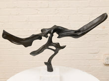 Load image into Gallery viewer, Abstract black metal sculpture with organic flowing branches and wings, displayed on a white pedestal against a white brick wall.
