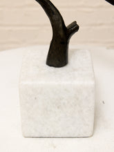 Load image into Gallery viewer, A close-up of a decorative sculpture featuring a dark brown faux-wood branch or antler mounted on a white marble cube base, set against a light beige brick wall background.
