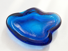 Load image into Gallery viewer, A translucent blue and dark navy glass dish with an organic, wavy shape, photographed on a white textured fabric background.
