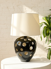 Load image into Gallery viewer, Vintage table lamp with glossy black ceramic globe base, circular pierced cutouts, and tapered neutral linen shade.
