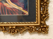Load image into Gallery viewer, Close-up of an ornate gold picture frame with floral carvings, holding a colorful painting, mounted on a white brick wall.
