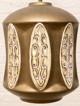 Load image into Gallery viewer, A close-up of a metallic bronze pendant light shade featuring three vertical oval cutouts with intricate scrollwork and warm yellow light glowing through.
