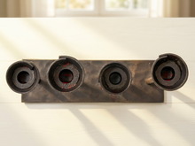 Load image into Gallery viewer, A rustic dark metal wall-mounted holder with four cylindrical sockets, shown on a white paneled wall with soft sunlight and window shadows.
