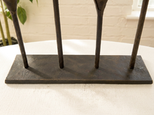 Load image into Gallery viewer, A rustic black cast iron candle holder with four upright legs and a rectangular base, shown on a white tablecloth in a home setting.
