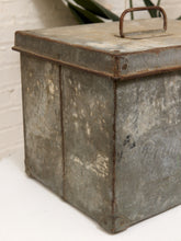 Load image into Gallery viewer, A distressed vintage galvanized metal storage box with a hinged lid and carrying handle, shown on a white surface against a white brick wall background.

