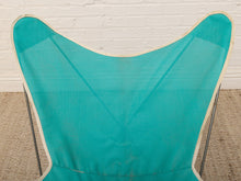 Load image into Gallery viewer, A vintage-style butterfly chair with a teal green mesh fabric backrest and a cream-colored fabric trim, supported by thin metal legs against a white brick wall and beige carpet.
