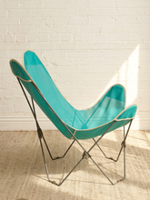 Load image into Gallery viewer, A mid-century modern butterfly chair with a vibrant turquoise mesh seat and backrest, supported by a thin silver metal frame, set against a white brick wall and a beige woven rug.
