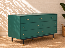 Load image into Gallery viewer, Image 3 of 4: A mid-century modern dresser in deep teal green with brass hardware and black legs with gold tips, set against a white brick wall with leaf shadows.
